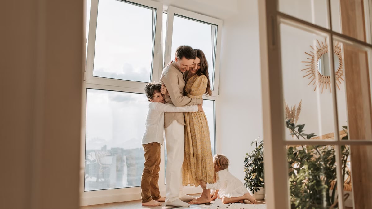 A happy family embracing near a large window in a bright, cozy room filled with natural light.