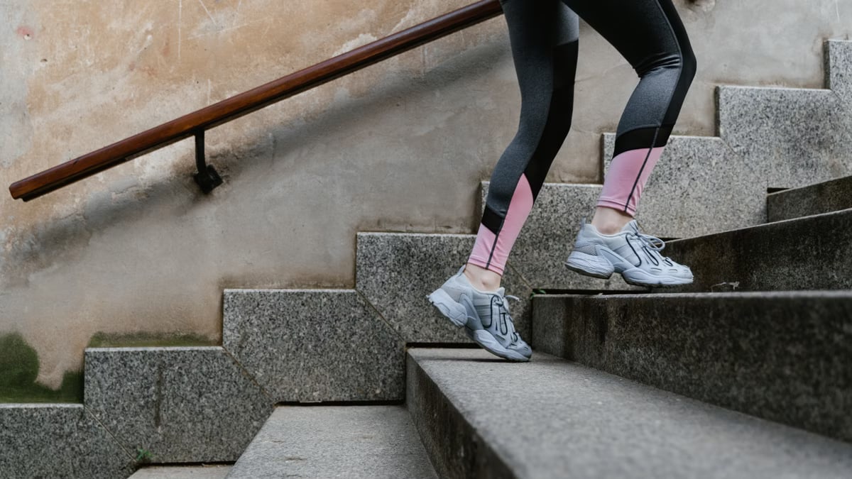 A woman in stylish leggings and sneakers climbing stairs outdoors, symbolizing fitness motivation.